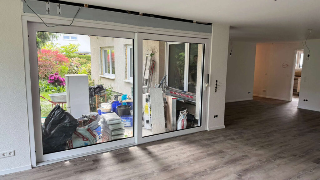 Vom renovierten Wohnzimmer mit Holzoptikboden eröffnet sich der Blick auf die Terrasse, wo noch Materialien und Werkzeuge lagern, HolzLand Beese Unna