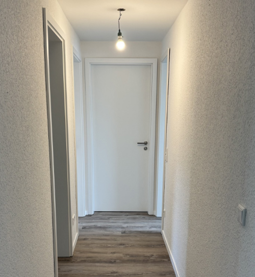 Ein schmaler Flur in der Wohnung mit Blick auf eine weiße Tür, erhellt von Glühbirnen an der Decke, HolzLand Beese Unna