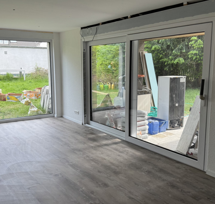 Renoviertes Wohnzimmer mit großen Fenstern und Blick in den Garten, Boden in Holzoptik, HolzLand Beese Unna