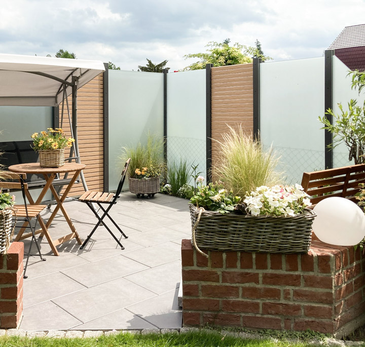 Gestaltete Terrasse: Glas- und Rhombus-Sichtschutz, Hollywoodschaukel, Sitzgelegenheiten, Pflanzen und geteiltem Mauereingang, HolzLand Beese Unna