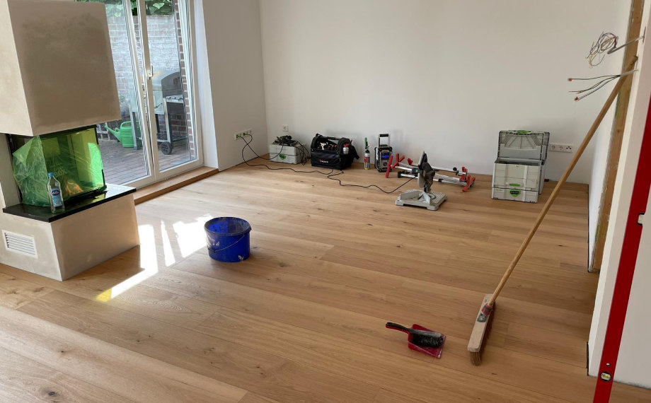 Das Wohnzimmer präsentiert sich als aufgeräumte Baustelle mit Holzoptikboden, einem Kamin und großen Fenstern zur Terrasse, HolzLand Beese Unna